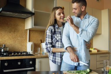Happy young couple embracing and talking in the kitchen while cooking breakfast at home in the morning