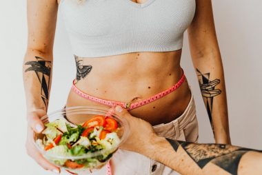 Fit woman measuring waist while holding a healthy salad bowl