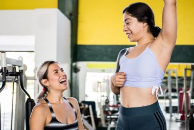 Two women in activewear sharing a joyful moment during a gym workout session.